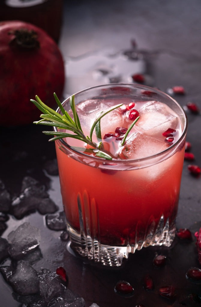 Peridot Pure Pomegranate Bergamot cocktail with rosemary sprig and arils for garnish